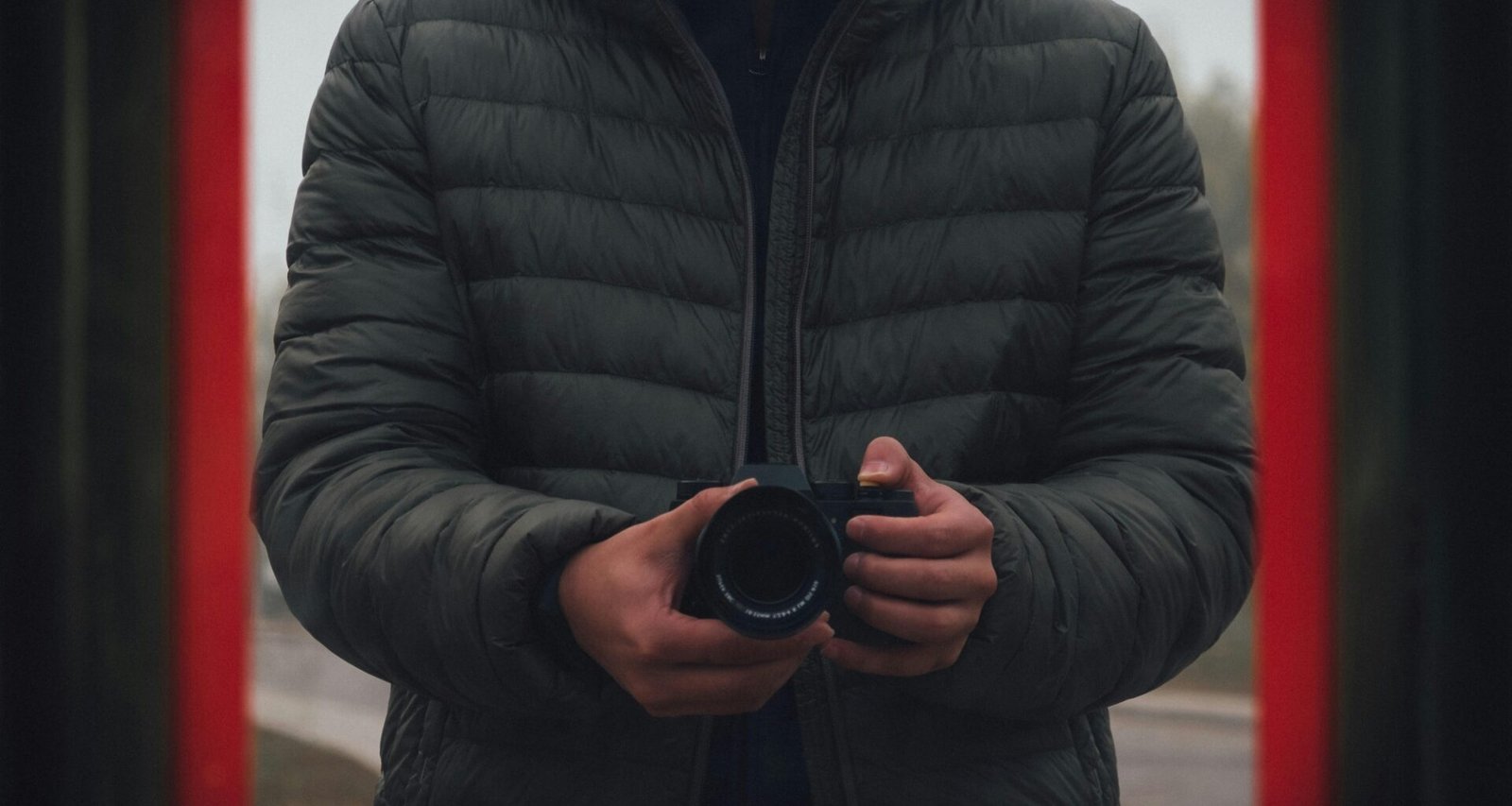 Mann in schwarzer Steppjacke mit DSLR-Kamera in der Hand, bereit zum Fotografieren, technikorientiertes Motiv