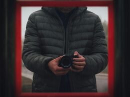 Mann in schwarzer Steppjacke mit DSLR-Kamera in der Hand, bereit zum Fotografieren, technikorientiertes Motiv