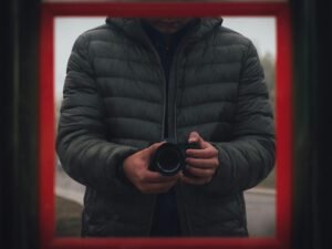 Mann in schwarzer Steppjacke mit DSLR-Kamera in der Hand, bereit zum Fotografieren, technikorientiertes Motiv