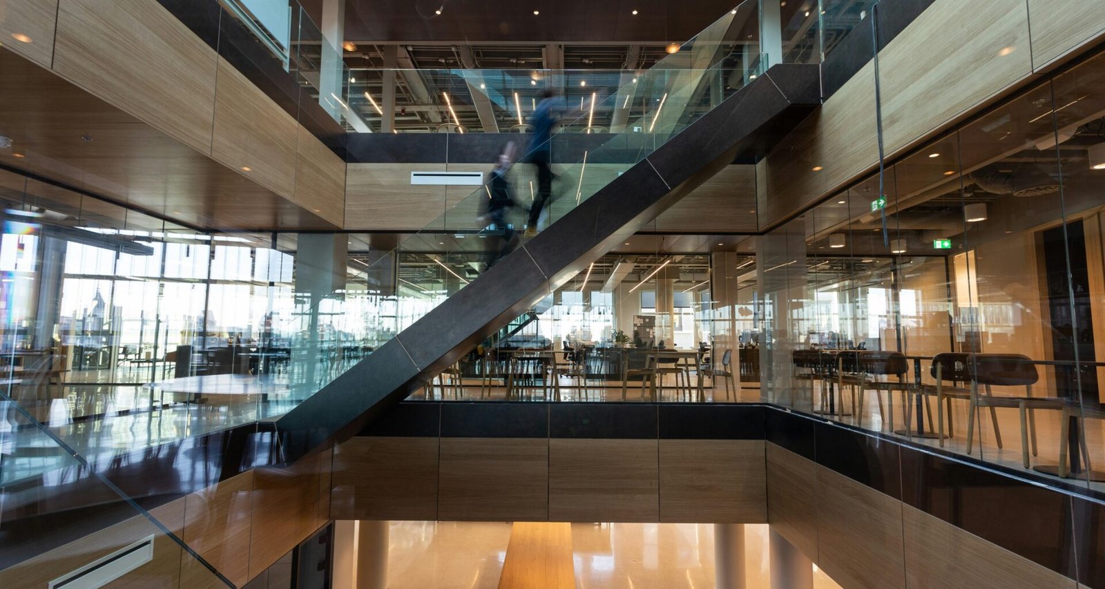 Ein Mann mit schwarzer Jacke geht auf einem braunen Holzfußboden durch einen offenen Innenbereich