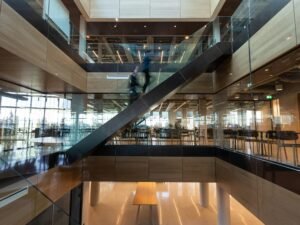 Mann in schwarzem Jackett läuft auf braunem Holzfußboden in einem modernen Innenraum. Fokus auf Arbeitsumgebung.