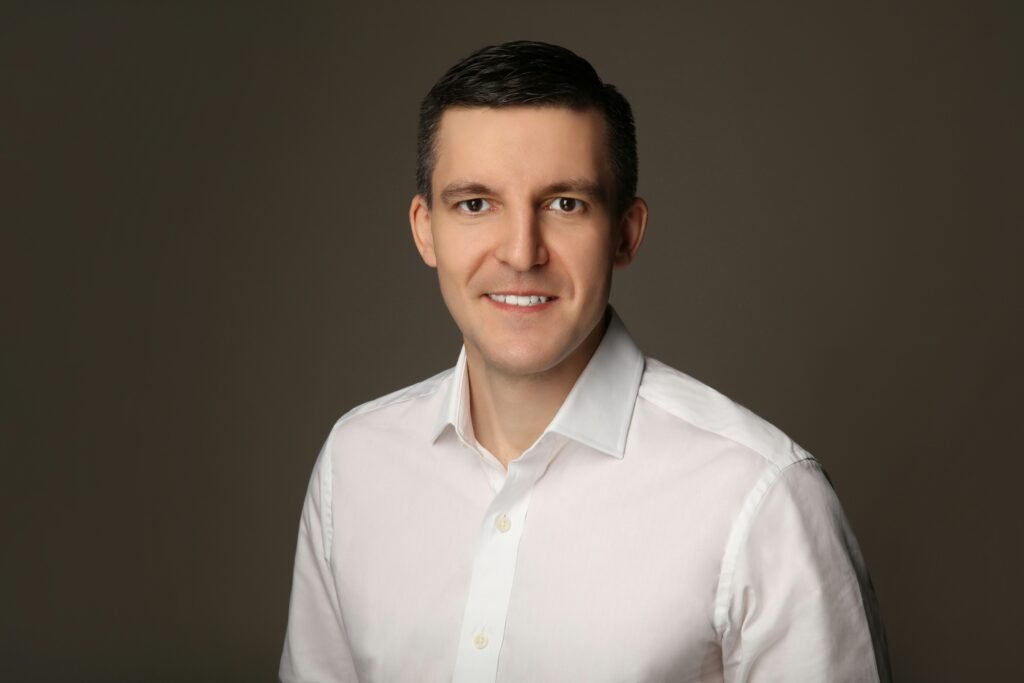 Lächelnder Mann mit weißem Hemd vor einem einfarbigen grauen Hintergrund, neutraler Business-Look