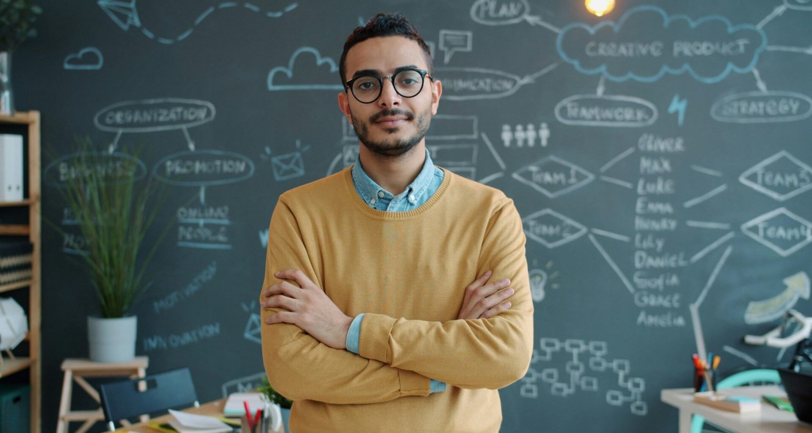 Mann mit Brille steht mit verschränkten Armen in einem modernen Büro vor einem Computertisch