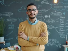 Mann mit Brille steht mit verschränkten Armen in einem modernen Büro vor einem Computertisch