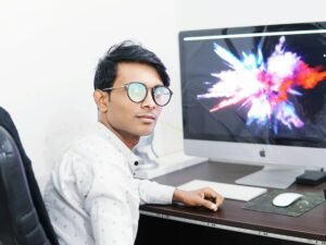 Ein Mann arbeitet konzentriert an einem iMac-Computer an einem hellen Schreibtisch im Büro.