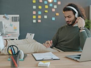 Mann sitzt am Schreibtisch und hört mit Kopfhörern Musik während der Arbeit, Fokus auf Technik und modernes Arbeiten