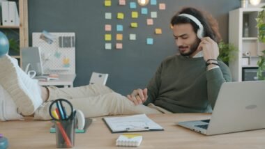 Mann sitzt am Schreibtisch und hört mit Kopfhörern Musik während der Arbeit, Fokus auf Technik und modernes Arbeiten