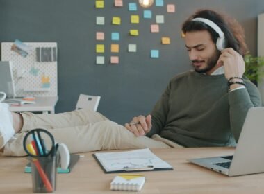 Mann sitzt am Schreibtisch und hört mit Kopfhörern Musik während der Arbeit, Fokus auf Technik und modernes Arbeiten