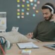 Ein Mann sitzt an einem Schreibtisch, trägt Kopfhörer und hört Musik, während er am Computer arbeitet.