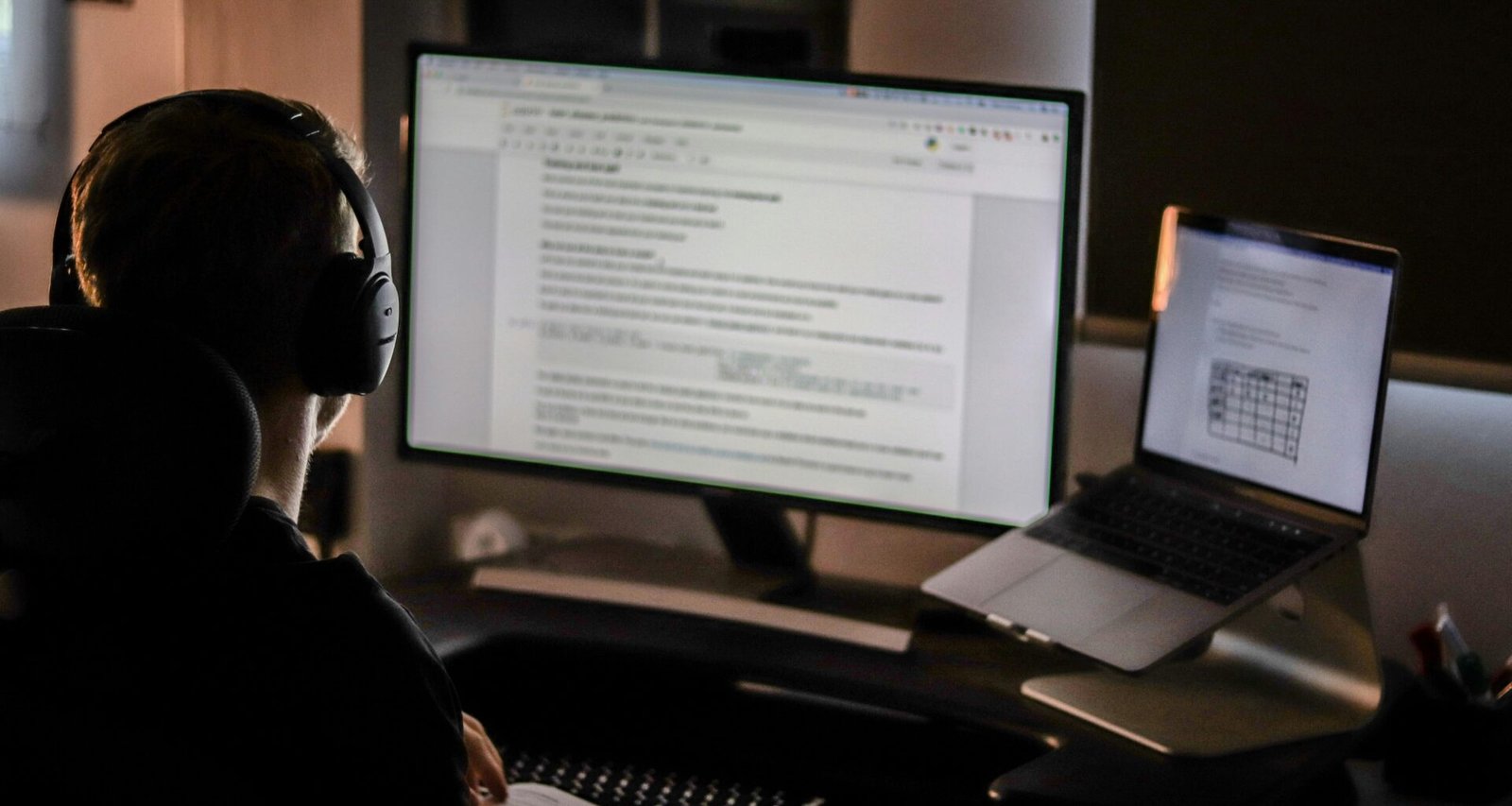 Mann mit Kopfhörern arbeitet konzentriert an einem Laptop an einem Schreibtisch in modernem Umfeld