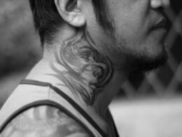 Mann mit sichtbarem Tattoo auf der rechten Wange, neutraler Hintergrund, aufgenommen von Mike Jumapao