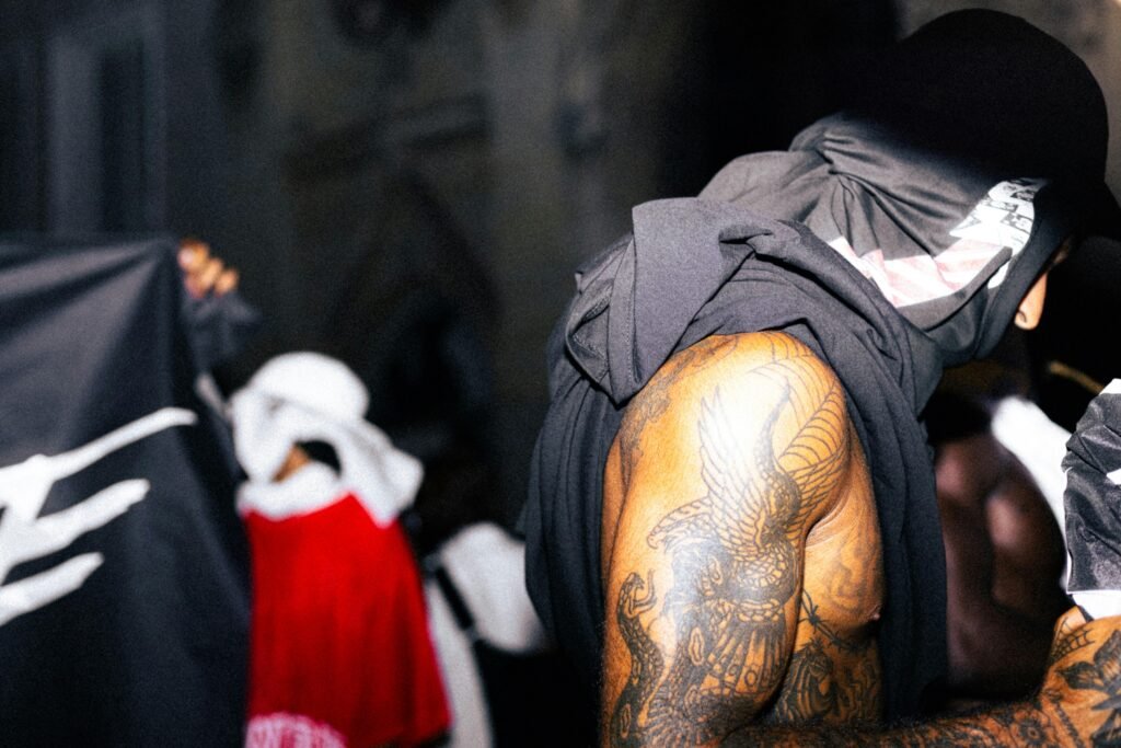 Tätowierter Mann sitzt in schwarzem und grauem Kapuzenpullover, urbaner Hintergrund, moderne Streetwear-Mode