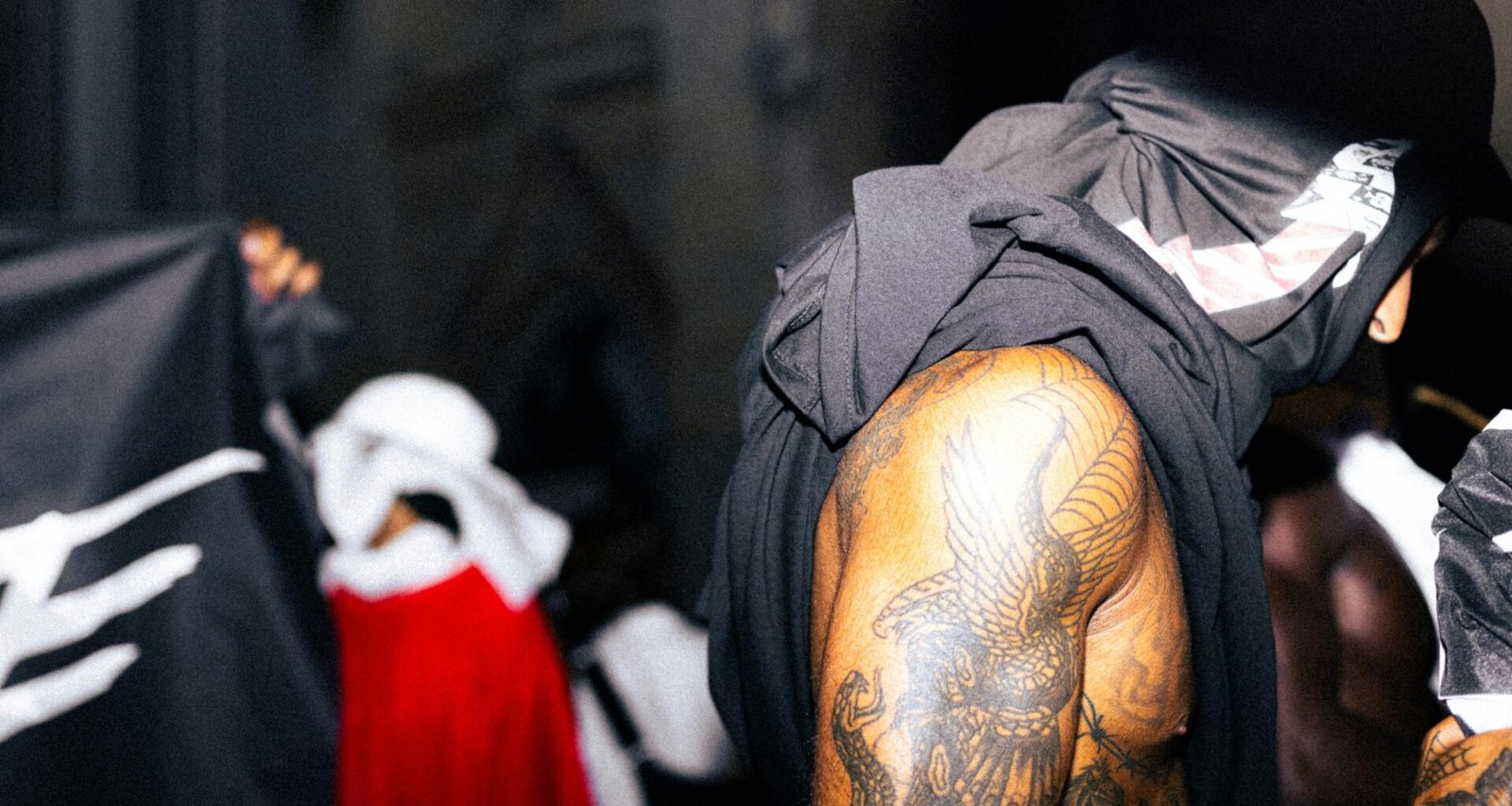 Tätowierter Mann sitzt in schwarzem und grauem Kapuzenpullover, urbaner Hintergrund, moderne Streetwear-Mode