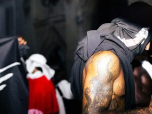 Tätowierter Mann sitzt in schwarzem und grauem Kapuzenpullover, urbaner Hintergrund, moderne Streetwear-Mode