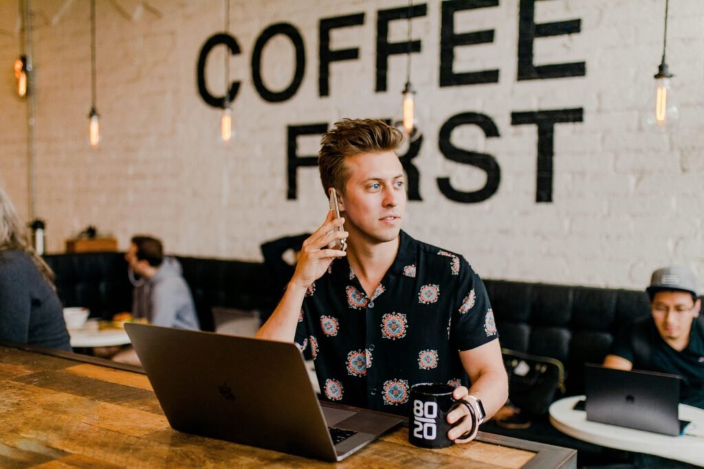Mann nutzt ein Smartphone während er an einem MacBook arbeitet, Fokus auf digitale Arbeitsweise im modernen Büroalltag