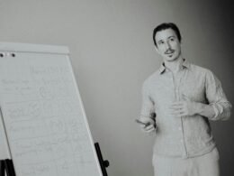 Ein Mann steht in einem modernen Büroraum an einem Whiteboard und präsentiert vor Kollegen im Meeting