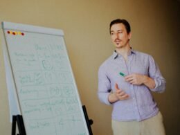 Mann präsentiert an einem Whiteboard mit Notizzetteln in einem modernen Besprechungsraum als Symbol für Teamarbeit