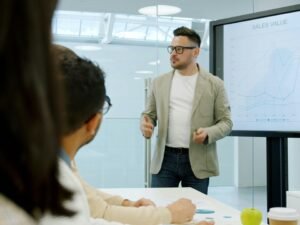 Mann zeigt Kollegen im Besprechungsraum Datenanalysen auf einem großen Bildschirm während einer Präsentation