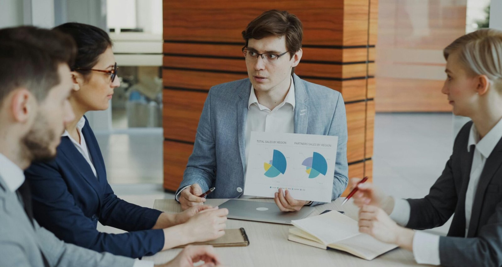 Mann präsentiert in einem modernen Konferenzraum verschiedene Diagramme vor Kollegen während eines Meetings