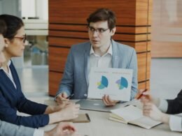 Mann präsentiert in einem modernen Konferenzraum verschiedene Diagramme vor Kollegen während eines Meetings