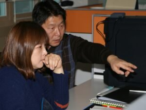 Ein Mann sitzt neben einer Frau, beide lehnen sich an einen weißen Tisch in einem hellen, modernen Büroraum.