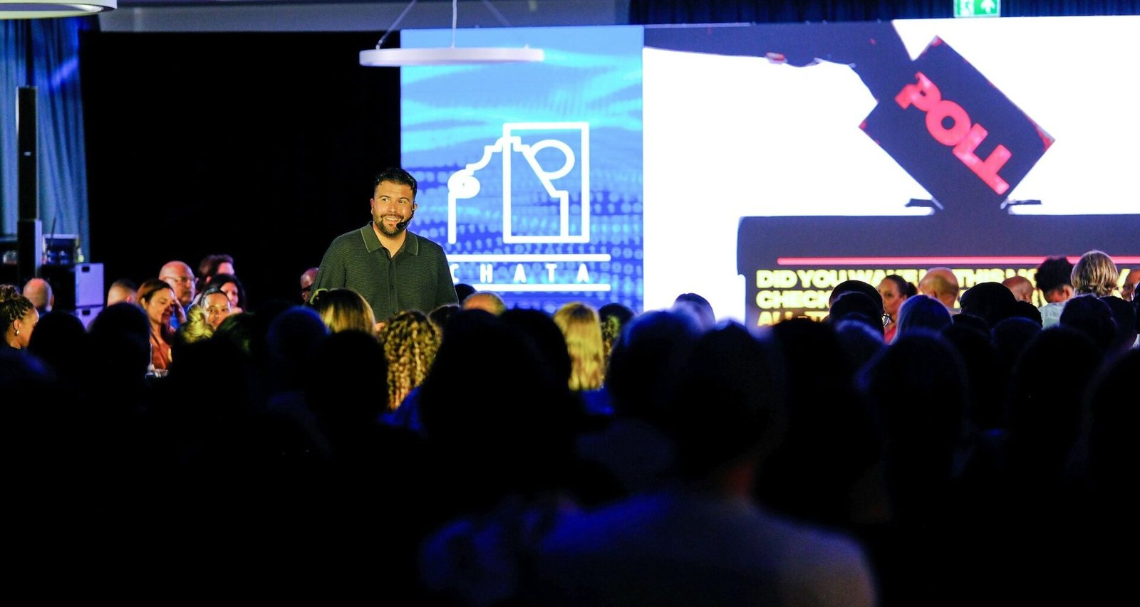 Mann spricht auf einer Bühne vor einem sitzenden Publikum, Lichtsituation in einem großen Saal, aufgenommen von Carlos Gil