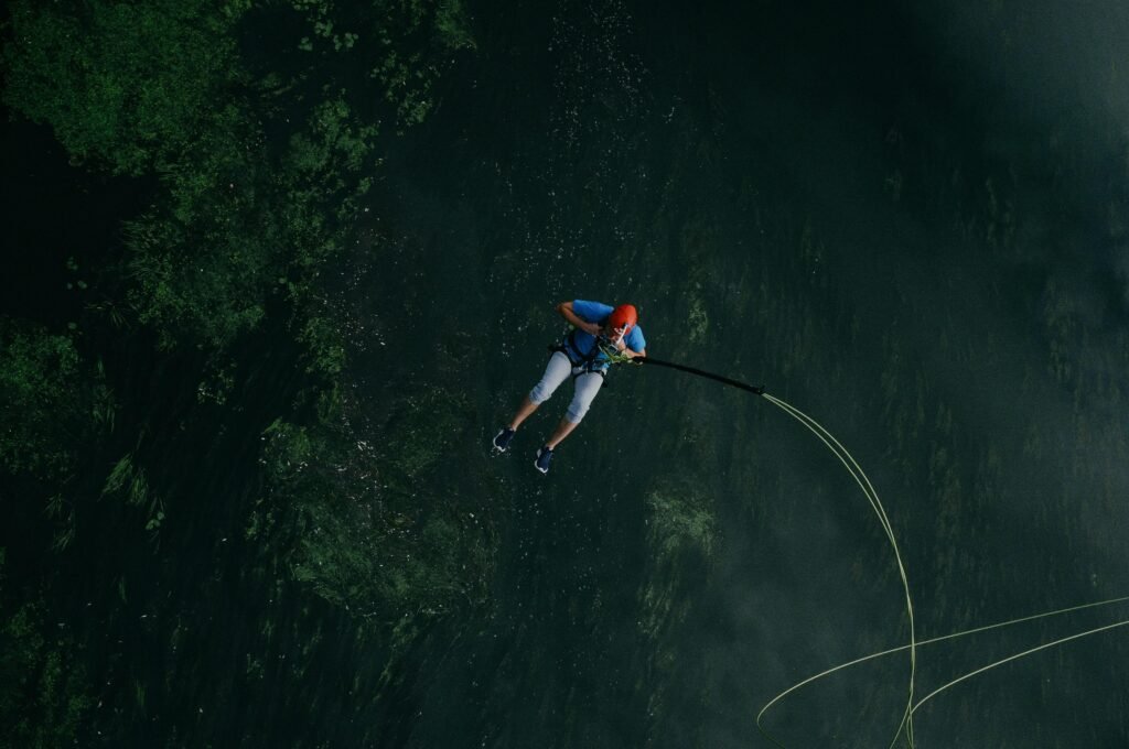 Ein Mann springt mit einem Sicherheitsseil von einer Klippe in einen See, aufgenommen im freien Gelände.