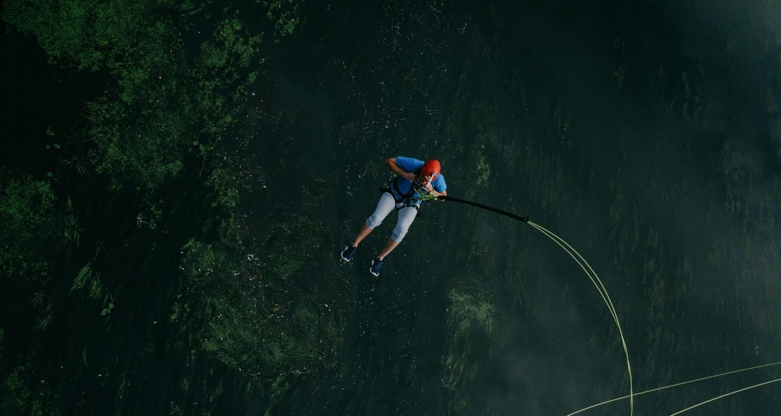 Ein Mann springt mit einem Sicherheitsseil von einer Klippe in einen See, aufgenommen im freien Gelände.