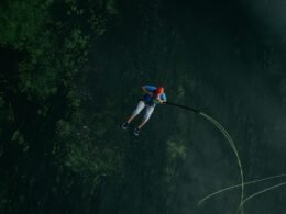 Ein Mann springt mit einem Sicherheitsseil von einer Klippe in einen See, aufgenommen im freien Gelände.