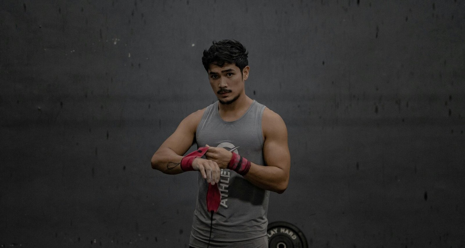 Mann steht in einem grauen Tanktop, aufgenommen vor neutralem Hintergrund, Fokus auf Oberkörper und Kleidung