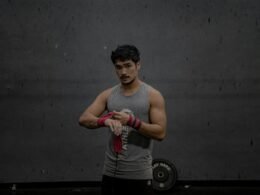 Mann steht in einem grauen Tanktop, aufgenommen vor neutralem Hintergrund, Fokus auf Oberkörper und Kleidung