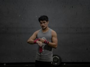 Mann steht in einem grauen Tanktop, aufgenommen vor neutralem Hintergrund, Fokus auf Oberkörper und Kleidung