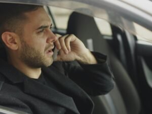 Mann sitzt im Auto und telefoniert mit dem Smartphone, typisches Bild für mobile Arbeit und Erreichbarkeit unterwegs.