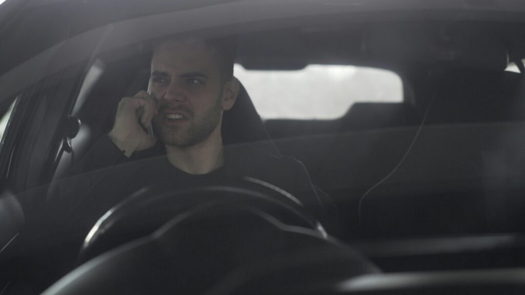 Mann sitzt am Steuer eines Autos und telefoniert mit dem Handy während der Fahrt, lenkt den Blick nach draußen