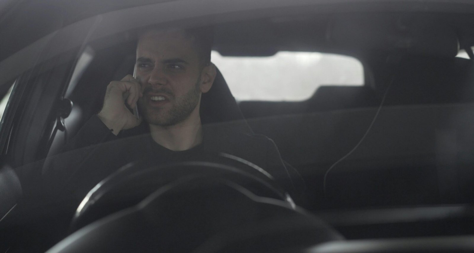 Ein Mann fährt ein Auto und hält ein Smartphone ans Ohr, während er am Steuer sitzt.