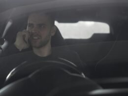 Ein Mann fährt ein Auto und hält ein Smartphone ans Ohr, während er am Steuer sitzt.