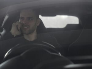 Ein Mann fährt ein Auto und hält ein Smartphone ans Ohr, während er am Steuer sitzt.