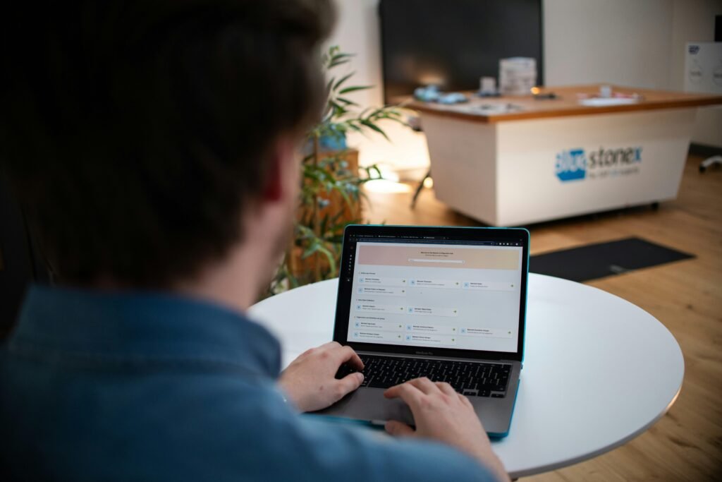 Mann arbeitet an einem Laptop, sitzt an einem weißen Tisch in moderner Umgebung, Fokus auf Hände und Tastatur