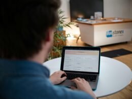 Mann arbeitet an einem Laptop, sitzt an einem weißen Tisch in moderner Umgebung, Fokus auf Hände und Tastatur