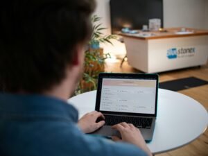 Mann arbeitet an einem Laptop, sitzt an einem weißen Tisch in moderner Umgebung, Fokus auf Hände und Tastatur