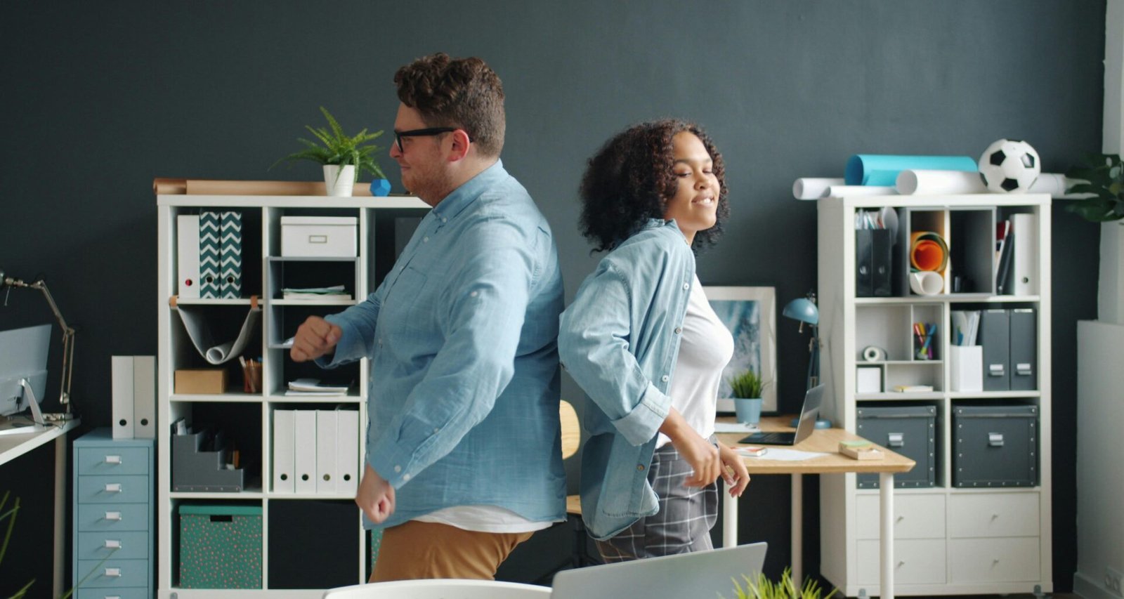 Mann und Frau sitzen im Büro Rücken an Rücken an ihren Arbeitsplätzen mit Laptops und Dokumenten.