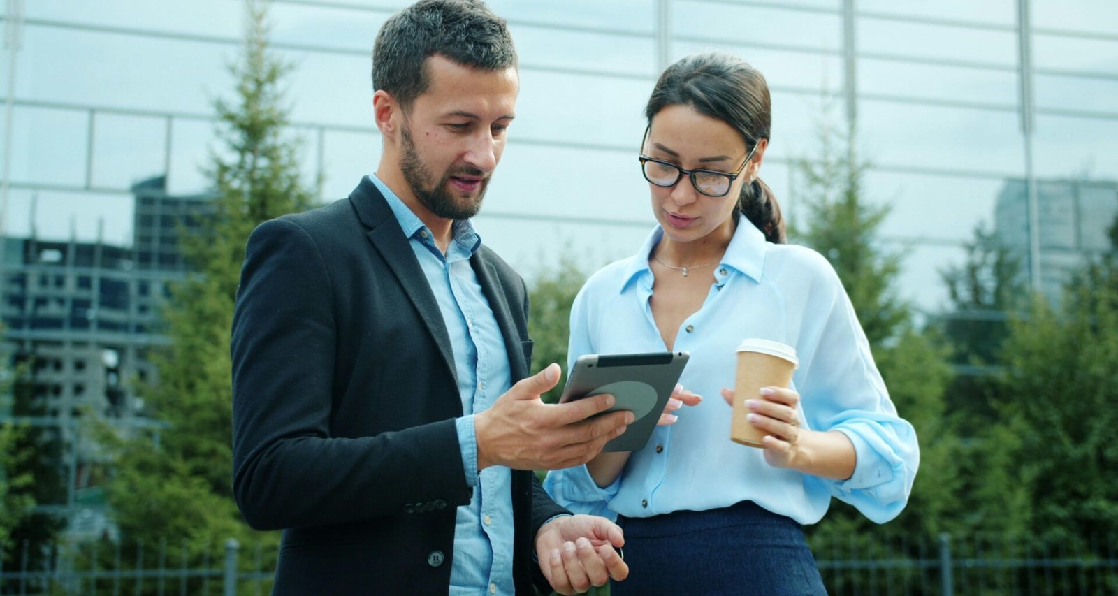 Ein Mann und eine Frau stehen vor einem Gebäude im Freien und schauen zusammen auf ein Tablet