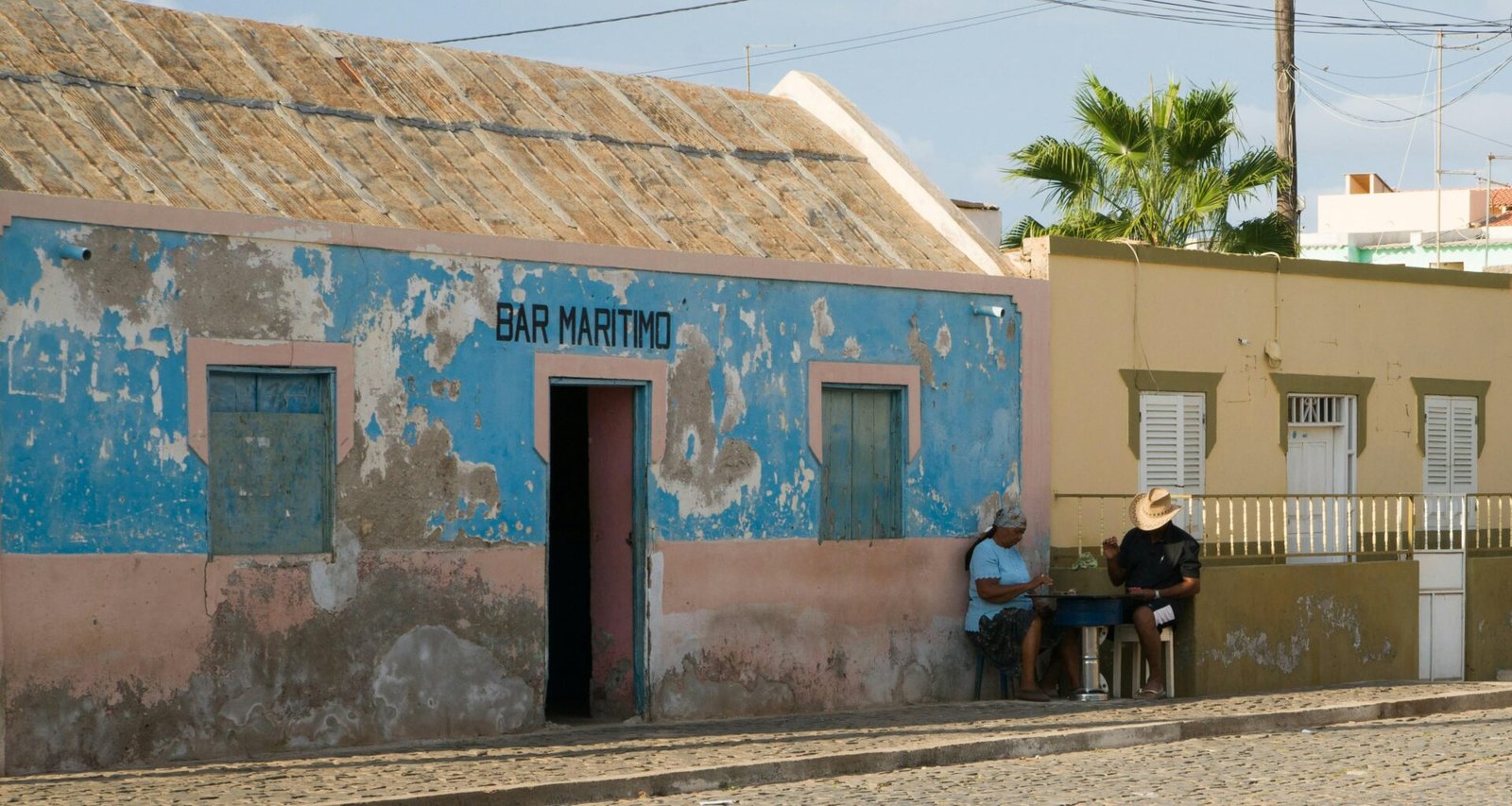 Ein Mann und eine Frau sitzen nebeneinander vor einem Haus direkt an einer Straße im Freien