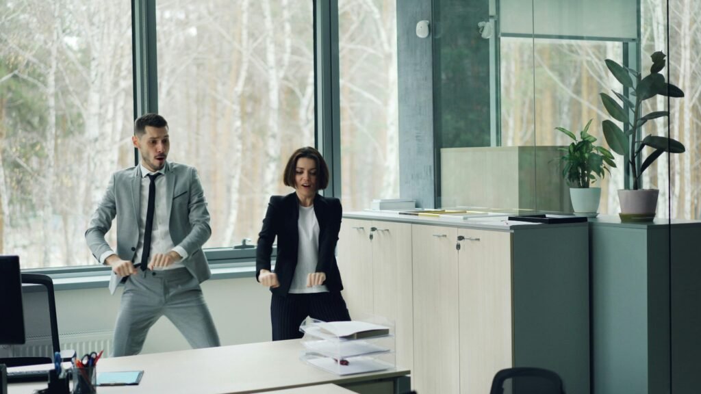 Ein Mann und eine Frau tanzen zusammen in einem offenen, modernen Büro zwischen Schreibtischen und Computern.