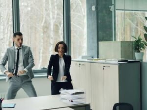 Ein Mann und eine Frau tanzen zusammen in einem offenen, modernen Büro zwischen Schreibtischen und Computern.