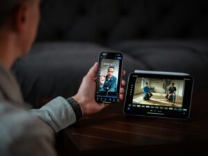 Mann nutzt sein Smartphone für einen Videoanruf, während er neben einem digitalen Monitor am Arbeitsplatz sitzt