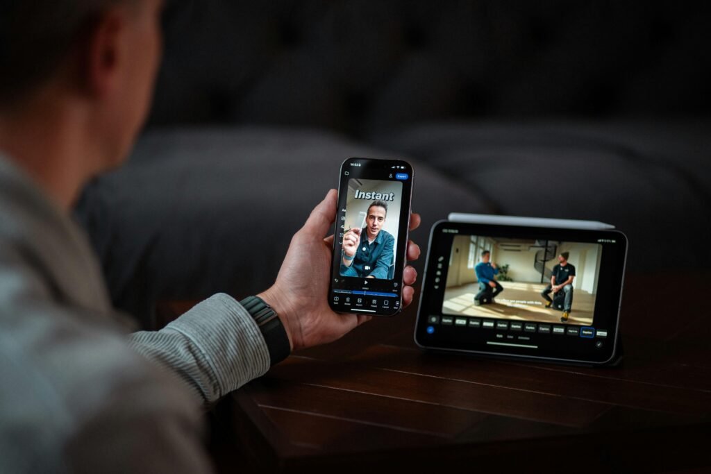 Mann sitzt neben digitalem Monitor und telefoniert per Videocall mit dem Smartphone in einem Büro.