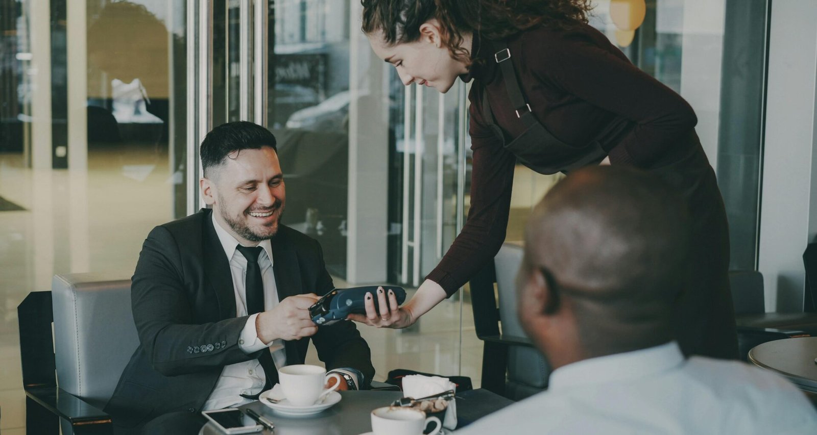 Ein Mann zahlt mit Kreditkarte an einem Café-Tisch; moderne digitale Zahlungsabwicklung wird dargestellt.