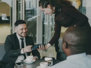 Mann sitzt an einem Café-Tisch und zahlt kontaktlos mit einer Kreditkarte direkt beim Servicepersonal.
