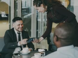 Ein Mann bezahlt mit einer Kreditkarte an einem Tisch in einem Café, moderne Zahlungsabwicklung im Alltag.